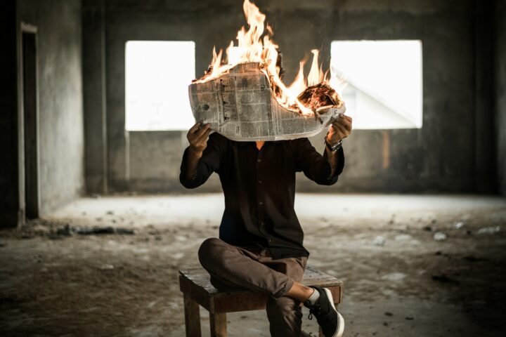 man sitting on chair holding newspaper on fire